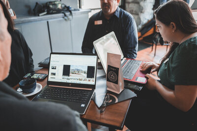 man sitting at a table with computers talking to other people