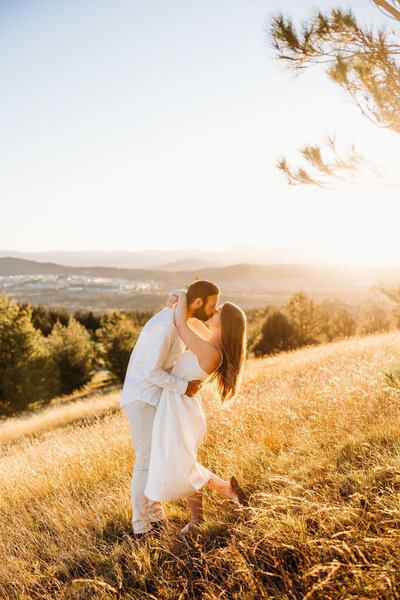 Stnning golden sunset at the National Arboretum Canberra with engaged couple kissing in the foreground. Photo by Acacia & Grace