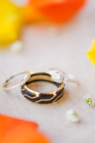 gold and black wedding bands surrounded by colorful flower petals