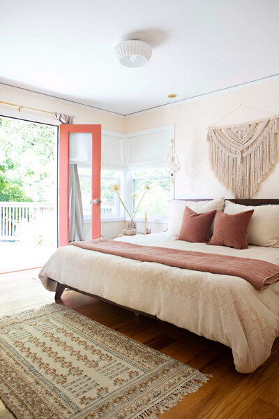 A bedroom featuring a large bed with a decorative macrame hanging on the wall above in and and a decorative rug on the floor in front of it representing an example of art deco boho interior design.