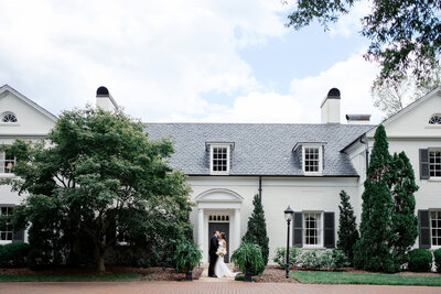 The couple has their first look at Boxwood Estate. You can see the beautiful, elegant grounds of the venue with trees and a historic manor behind them. 