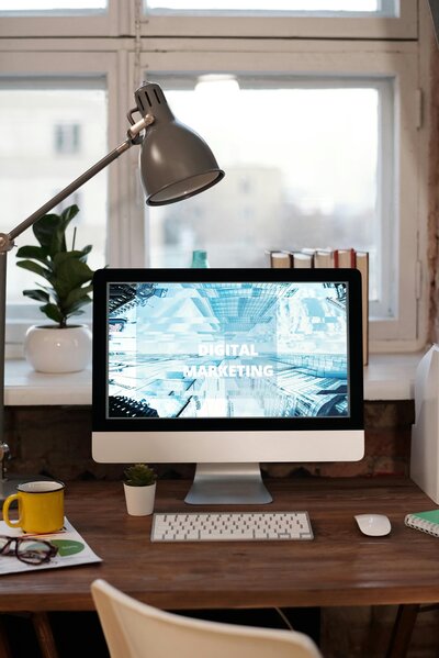 an image of a mac desktop computer at a desk with a keyboard, mouse, and coffee cup on a wooden desk in front of a window