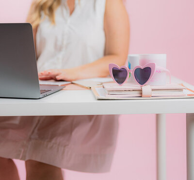 A desk with pink sunglasses and Amy faded in the background