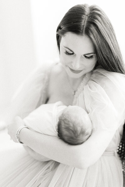 Light filled black and white newborn photo of a mother wearing a tulle gown as she holder her newborn baby close,