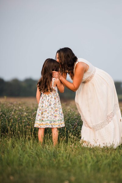 Woman whispering to a young girl during a family photoshoot in a field.