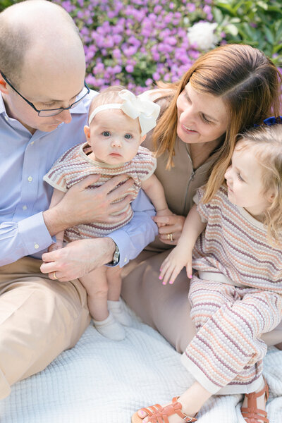 Portrait of a family sitting on a white quilt in front of a bed of flowers taken by louisville family photographer missy marshall