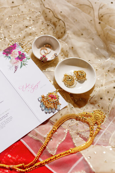 Rings, jewelry, and wedding invitations laid on top of a wedding dress 