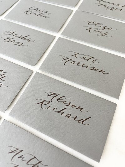 Grey escort card envelopes with walnut ink calligraphy
