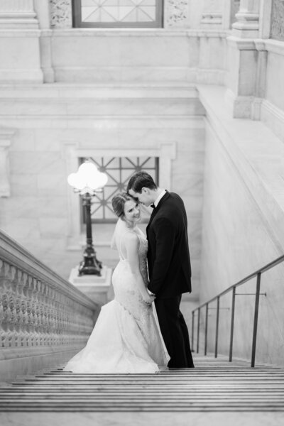 A bride in a flowing white dress and her husband in a black suit hold each other and smile at the camera