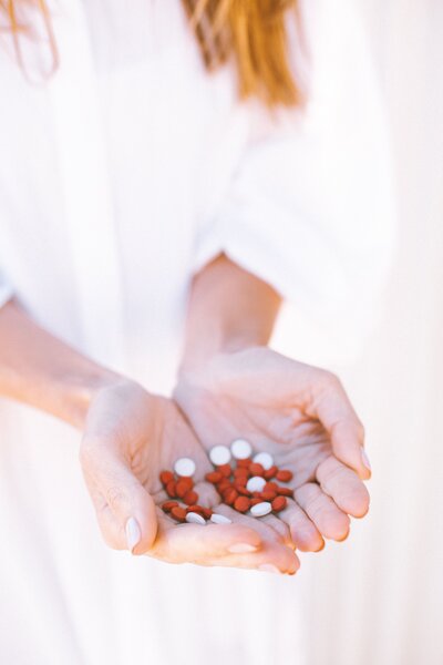 Woman in white blouse holds a bunch of red and white pills and medications in her hands