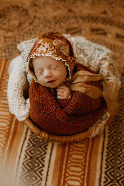 Photo of a newborn baby girl posed in a newborn basket with a pretty wrap and bonnet.