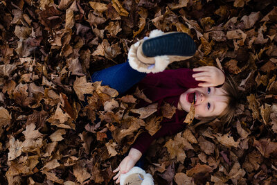 Kid being silly in the leave during their family photography session in the fall