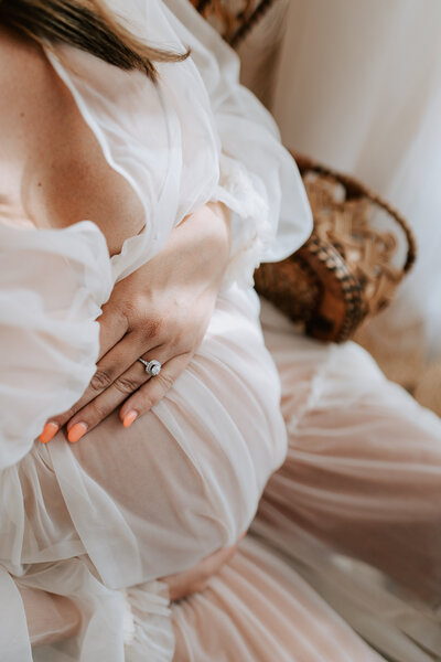 Beautiful maternity portrait showing a glowing expectant mother cradling her baby bump while standing in a lush garden during sunset. The mother-to-be wears an elegant white dress, radiating joy and anticipation. Professional maternity photography capturing the essence of pregnancy and maternal happiness