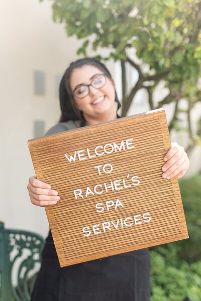 Rachel Smith of Rachel's Spa Services outside spa holding a welcome sign in Boardman, Ohio.