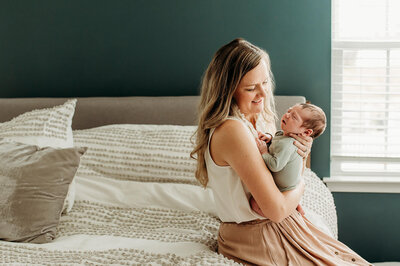 Woman in blue dress sitting in nursery rocking chair holding newborn kissing man in grey shirt and blue jeans near Baltimore Maryland