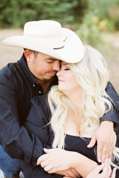 man with cowboy hat and black shirt embracing fiance in black dress eyes closed