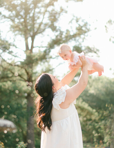 Mother dressed in white holds baby up in the air, at golden hour, by Amsterdam-based photographer.