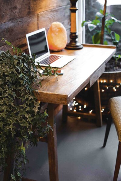 a cozy wooden desk with a laptop, a plant, twinkle lights, and a salt lamp