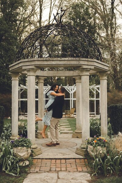 Engaged couple embracing under a romantic stone gazebo during a spring session