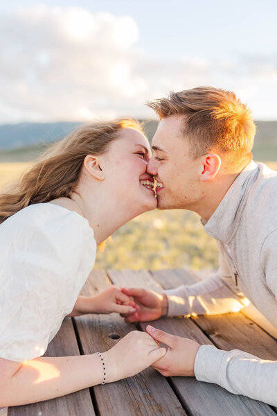 Sweet couple sharing an intimate kiss across a picnic table during their engagement session in Wyoming, perfectly capturing their love against a scenic backdrop.