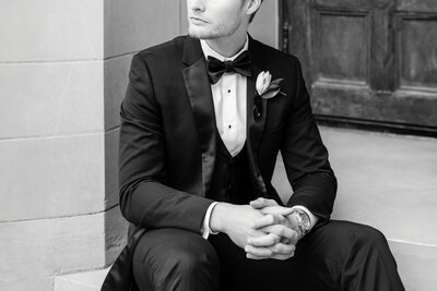 black and white photo of groom sitting down with hands clasped together and looking to the side