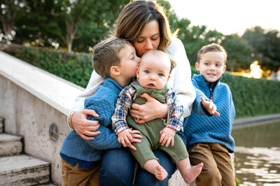 Mom holding her three young boys and kissing them during an outdoor family session with Allison Krogness.