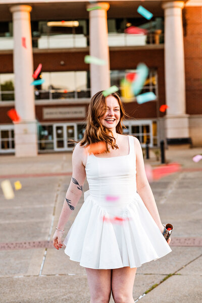 Senior girl wearing white dress spinning around as confetti rains down on her outside the MTSU library