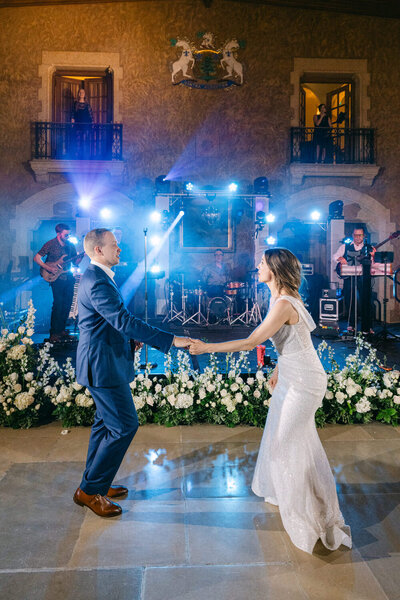 Bride and groom enjoying their first dance in Mount Stephen Hall at the Fairmont Banff Springs Hotel laughing together with the live band performing behind them and blue stage lighting creating an energetic atmosphere