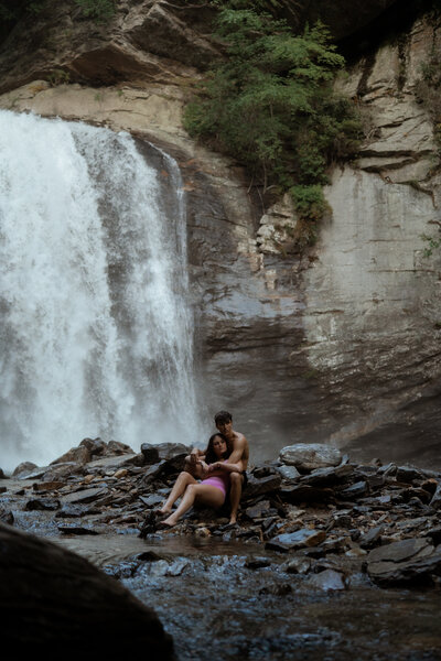 couple sitting at the base of Looking Glass Falls in swimsuits in Asheville North Carolina