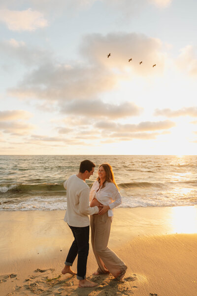 a man and pregnant woman on the beach during sunset