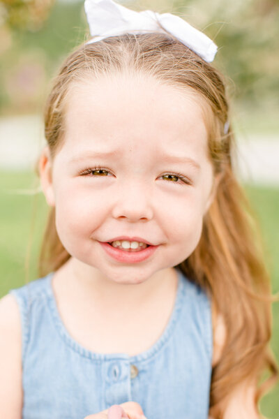 Young girl wearing a bow smiles at camera during a family session in Braselton