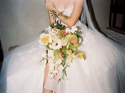 A modern and artistic bridal portrait captured in Dallas-Fort Worth, featuring a bride in an ethereal gown, reclining against a vintage wooden dresser, surrounded by lush florals.
