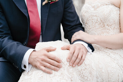 A newlywed couple clasps hands, on their wedding day, sharing a special tender moment