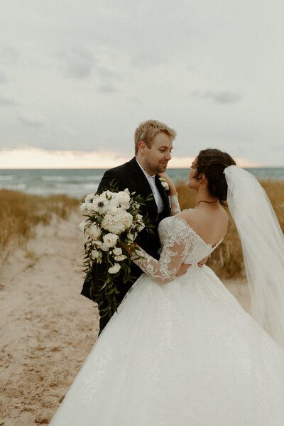 Married couple holding each other on the beach at Ludington State Park on Lake Michigan.