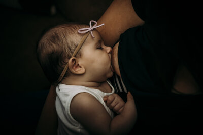Baby wearing a bow headband breastfeeding during a quiet postpartum moment