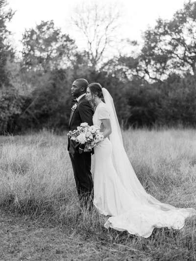 Black and white photo of bride and groom standing in a field