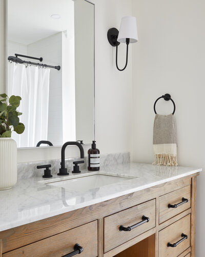 Bathroom with lovely marble couter, large mirror, black hardware, and light wooden under-sink cabinets.