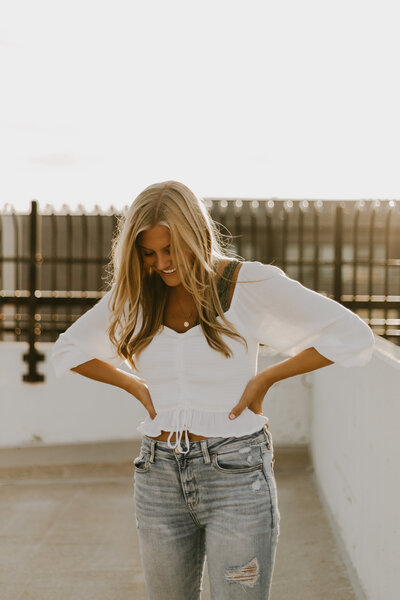 Natural senior photo of a girl in a white blouse and blue jeans on the roof of a parking garage in Grand Rapids.