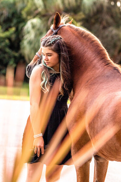 girl in black dress hugging her pony and looking over her shoulder