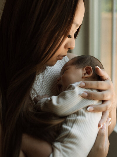 A tender moment between mother and baby by the window, bathed in soft morning light.
