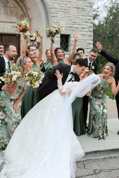 groom dips bride while bridal party cheers