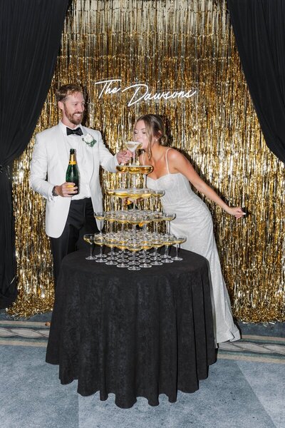 Couple with champagne tower and custom backdrop at Hotel del Coronado, designed by Thater Made, a luxury wedding and event producer in San Diego, CA.