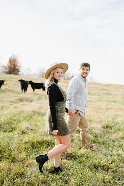 couple walking through field with cows by nashville engagement photographer