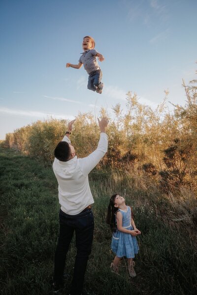 A man twirls his fiancée in a prairie field by a lake at sunset.