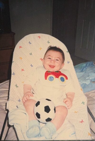 A baby in a rocker with a soccer ball