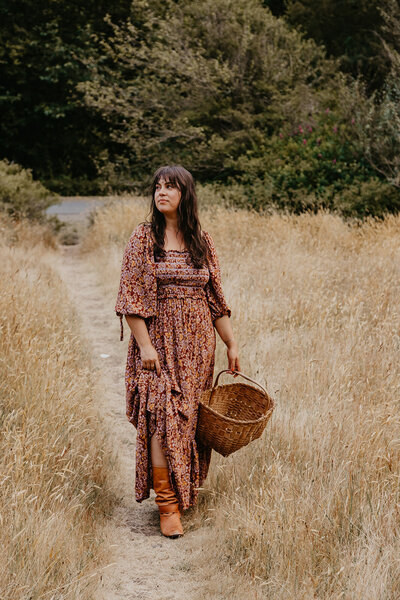 brand strategist and website designer standing in a grassy field holding a basket wearing a full length dress