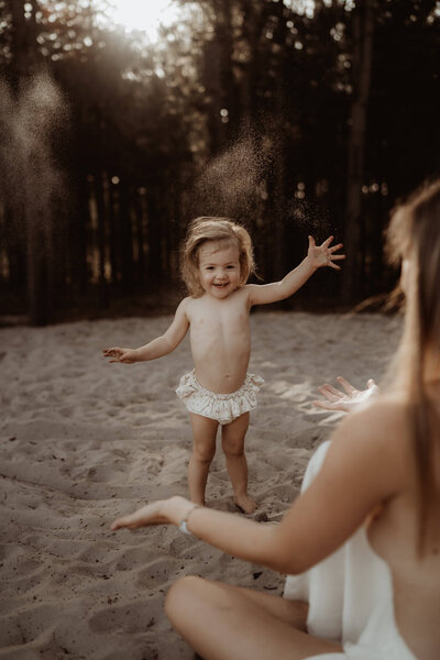 Kindje dat tijdens een fotoshoot met mama in het zand aan het spelen is