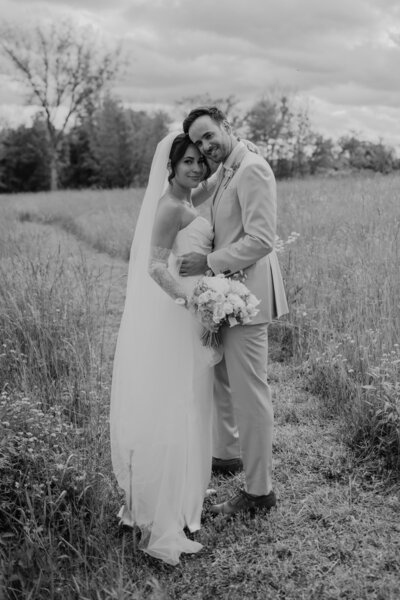 Black and white image of bride and groom, holding each other in a field
