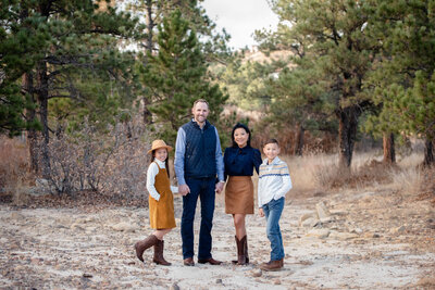 A family of 4 stand in a mountain trail holding hands at sunset for a Colorado Springs family photographer