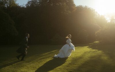 A joyful moment of a woman playing tag with her husband on grassy fields, captured during a stunning golden-hour sunset.
